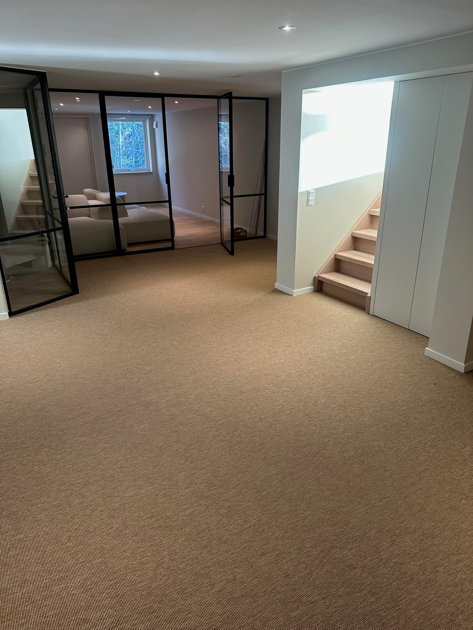 Källarvåning med sisalmatta, svart glasparti och trappa i ek